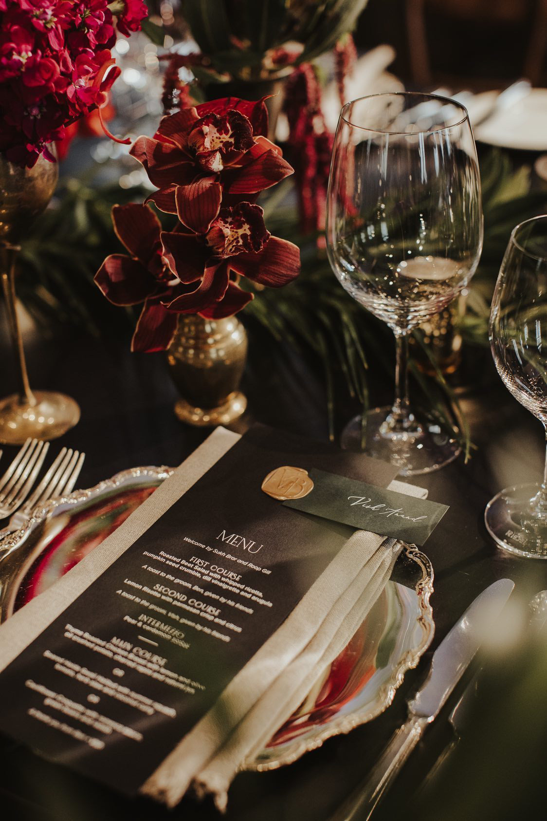 A sophisticated wedding table setting featuring a minimalist black menu, a forest green name place card, and a bespoke wax seal. This elegant stationery suite by Heirloom Stationery showcases high-contrast typography and refined finishing details.
