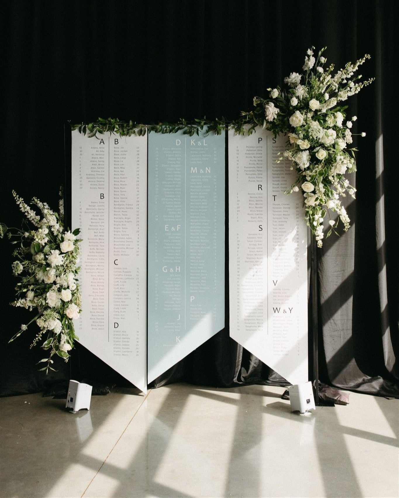 A contemporary angle-cut wedding seating chart with a sharp, geometric silhouette. This bespoke guest list signage by Heirloom Stationery features clean lines and a sophisticated layout for a modern event aesthetic.